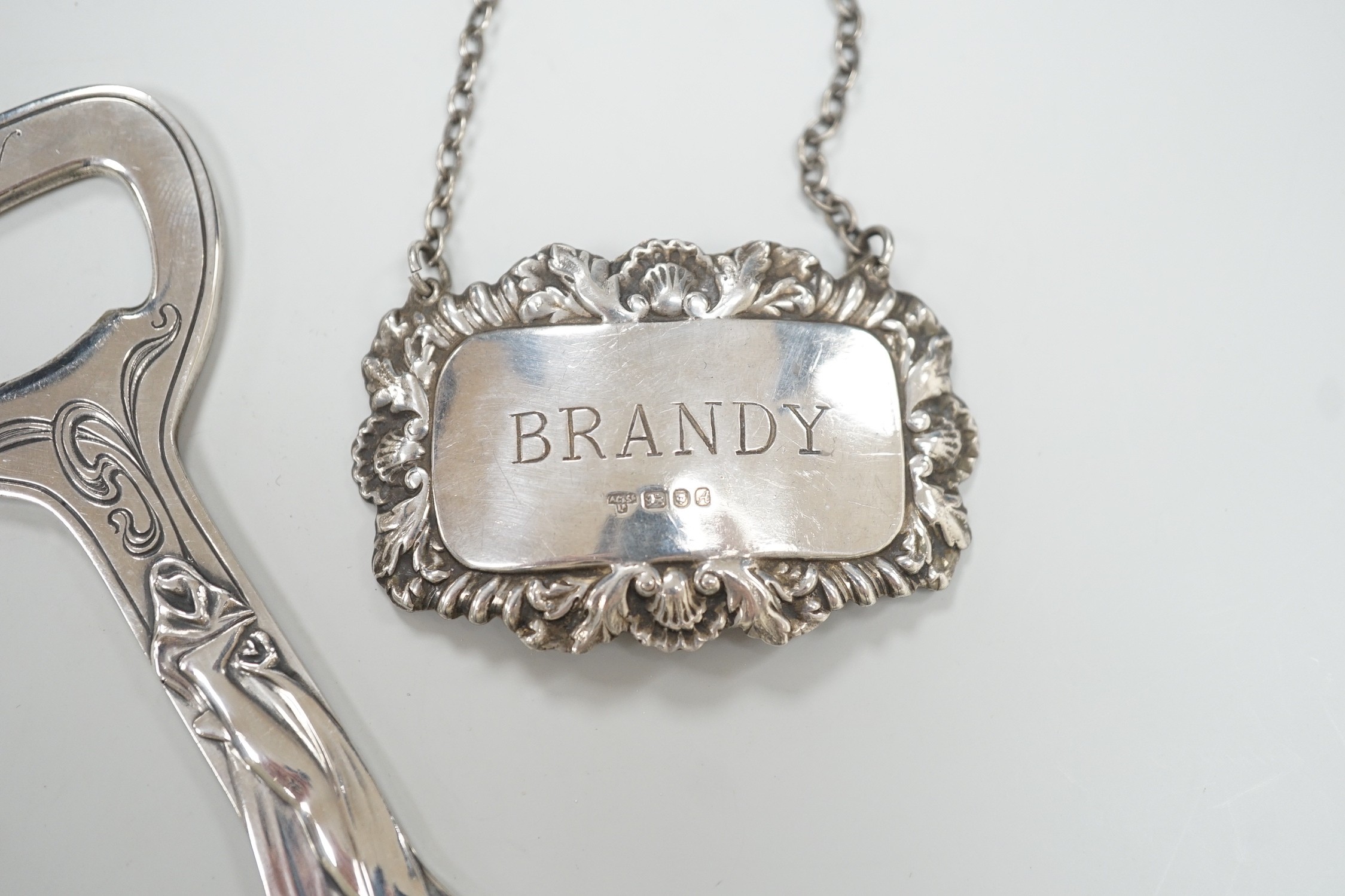 A pair of Queen Elizabeth II silver wine labels, 'Sherry & Brandy', A. Chick & Sons, Ltd, London, 1975 and an Art Nouveau style silver plated bottle opener.